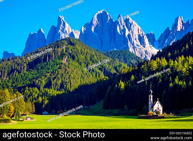 Small white church with among green lawns on the sunset. The village Santa Maddalena in the Val di Funes Valley. Italy, Tyrol