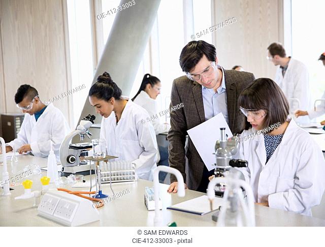 Science professor helping college student conducting scientific experiment in science laboratory classroom