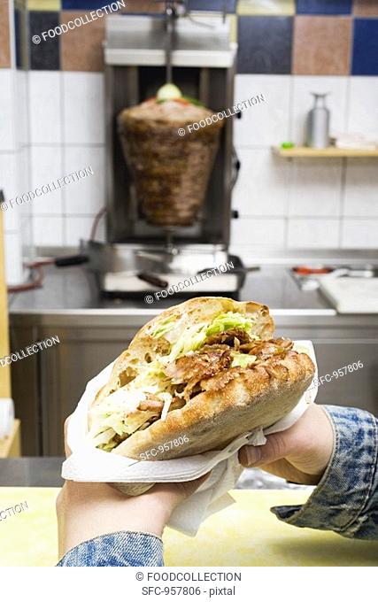Hands holding a döner kebab in a snack bar