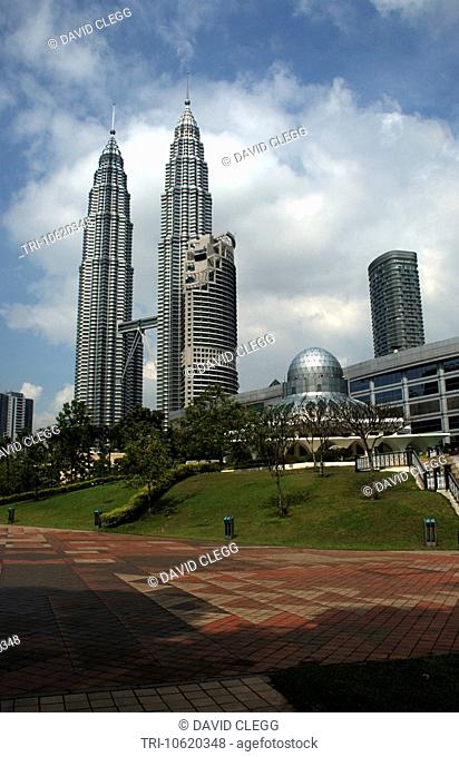 Petronas Twin Towers seen across park with the round dome of the Asy-Syakirin mosque seen to right grass and trees around mosque with red and fawn tiled...
