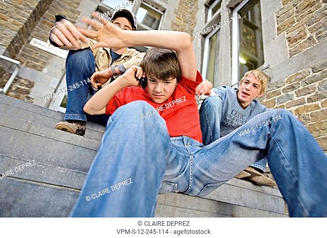 Low angle view of a teenage boy talking on a mobile phone and two teenage boys hitting him from behind