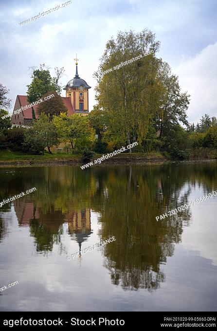 16 October 2020, Brandenburg, Wriezen/Ot Frankenfelde: The church of the village and trees are reflected in the water of a pond