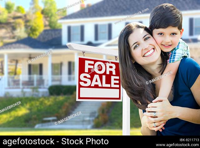 Young mother and son in front of for sale real estate sign and house