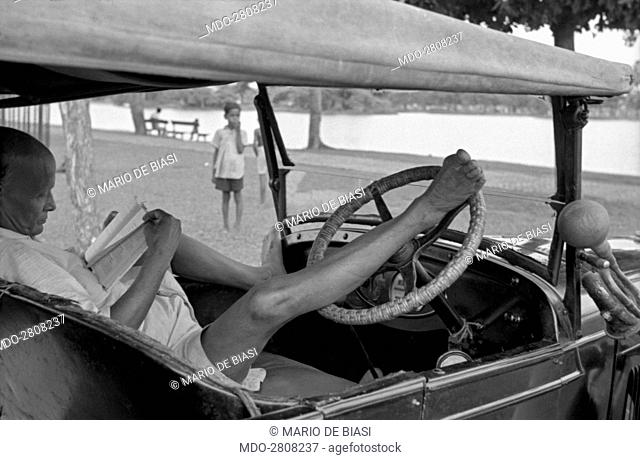 A man reading a book on a car. Kolkata, 1962
