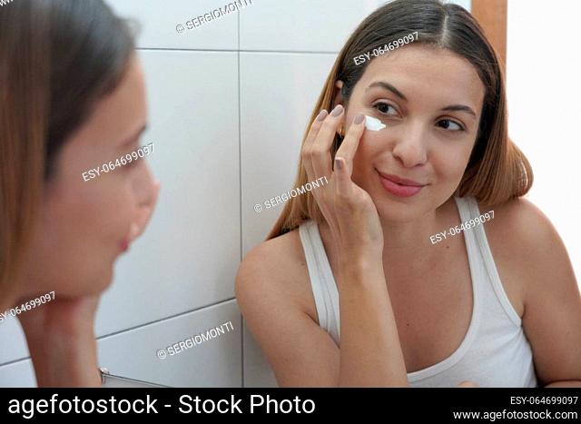 Beauty routine at home. Portrait of beautiful girl applying cream under eye with finger. Dark circles and anti-wrinkle concept