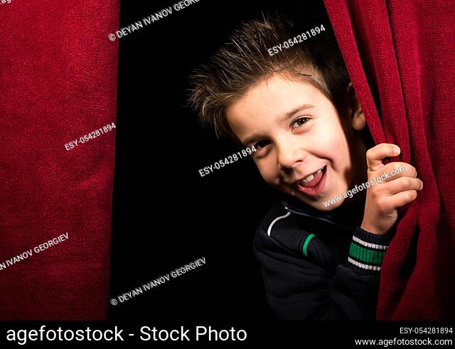Child appearing beneath the curtain. Red curtain