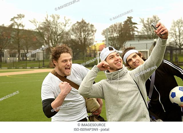 Three male soccer players taking celebration smartphone selfie