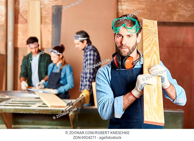 Kompetenter Schreiner mit Holzbrett und Arbeitsschutz in Werkstatt