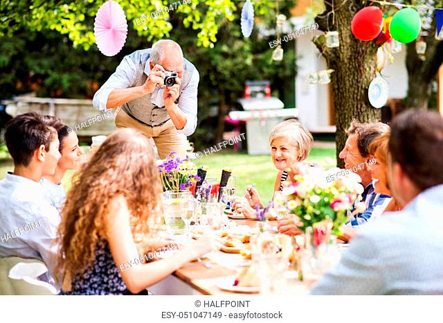 Family celebration outside in the backyard. Big garden party. Grandfather taking photo with a camera