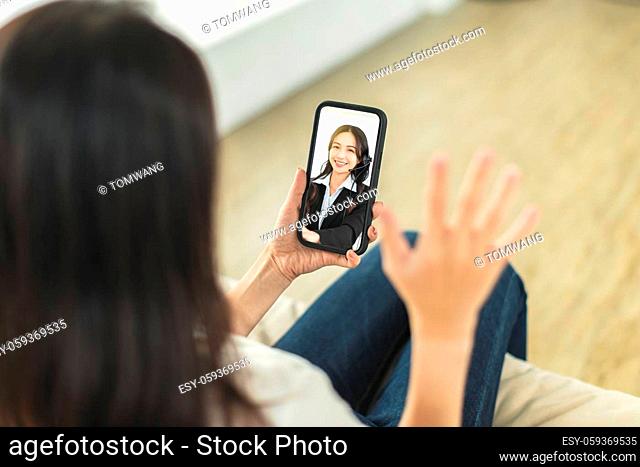 Young woman sitting on sofa holding mobile phone, making video call, discussing with company colleagues in telecommuting