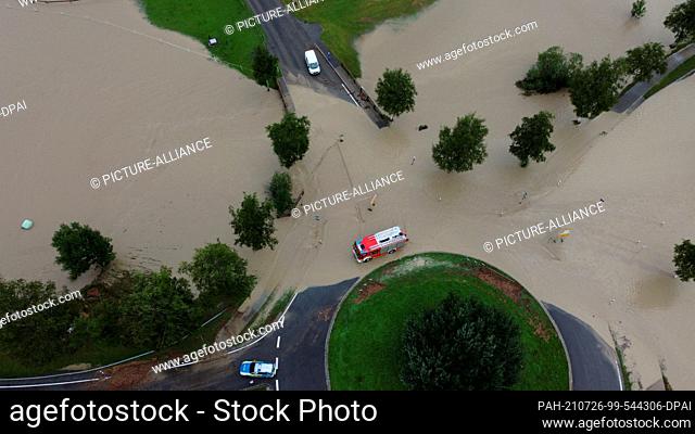 26 July 2021, Bavaria, Rettenberg: A fire engine drives through the high standing water at a roundabout outside the town (shot with a drone)