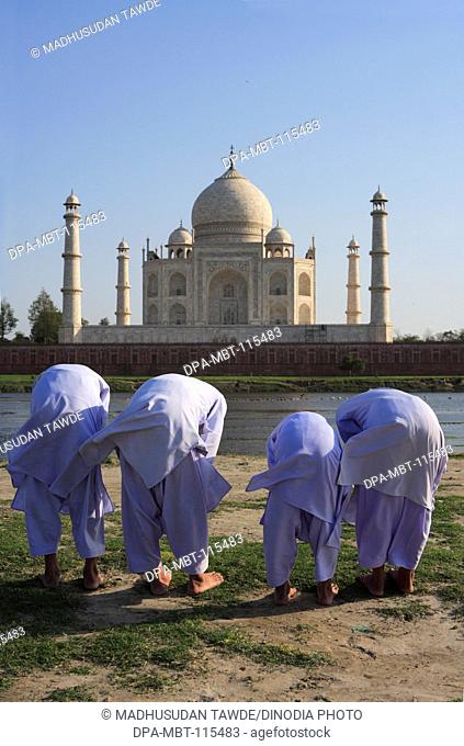 Young muslim boys performing religious prayer Namaz in front of Taj Mahal Seventh Wonders of World on south bank of Yamuna river , Agra , Uttar Pradesh