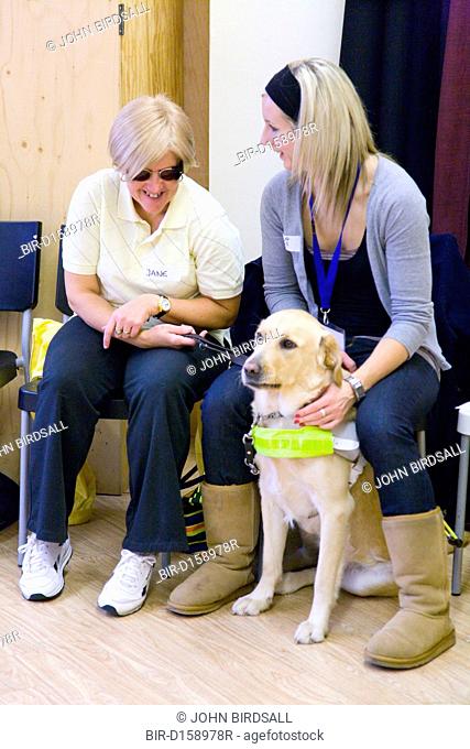 Visually impaired woman with a guide dog talking to a class assistant at NRSB activity day at their centre on Ortzen Street