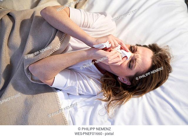 Woman lying in bed blowing her nose