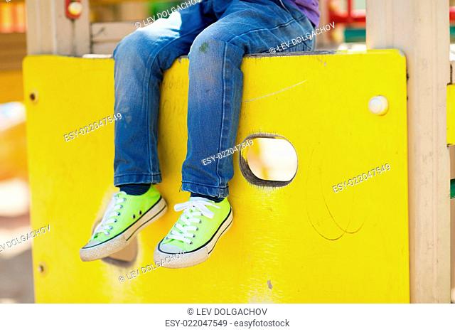 summer, childhood, leisure and people concept - close up of little boy legs sitting on climbing frame at children playground