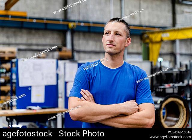 Contemplating male technician looking away with arms crossed at factory