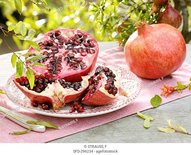 Pomegranate, cut into pieces, on plate beside whole fruit