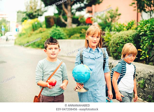 Group of three funny kids wearing backpacks walking back to school. Girl and boys enjoying school activities. Globe, lunch box, red apple and bag accessories