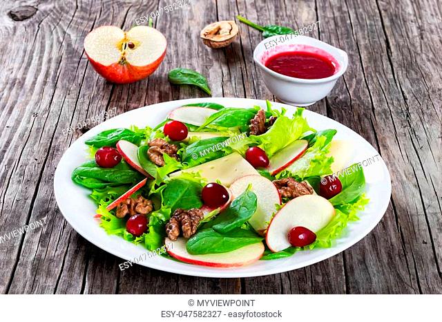 apple, spinach, cheese, lettuce leaves Frise, caramelized walnuts, cranberry salad on a white plate with knife and fork, cranberry dressing on the background