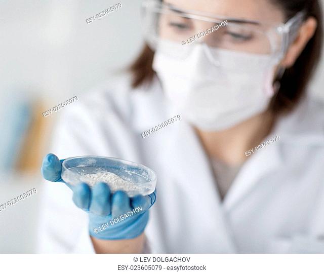 science, chemistry, biology, medicine and people concept - close up of young female scientist holding petri dish with powder in clinical laboratory