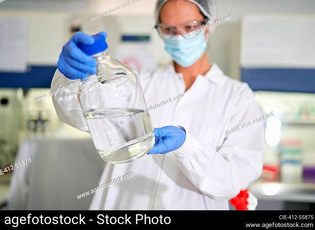 Female scientist in face mask and glove examining liquid in laboratory