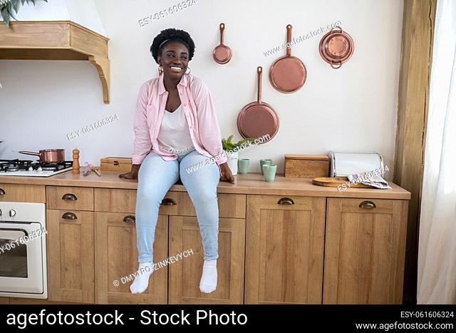 Leisure. A woman in pink shirt sitting on the table in the kitchen