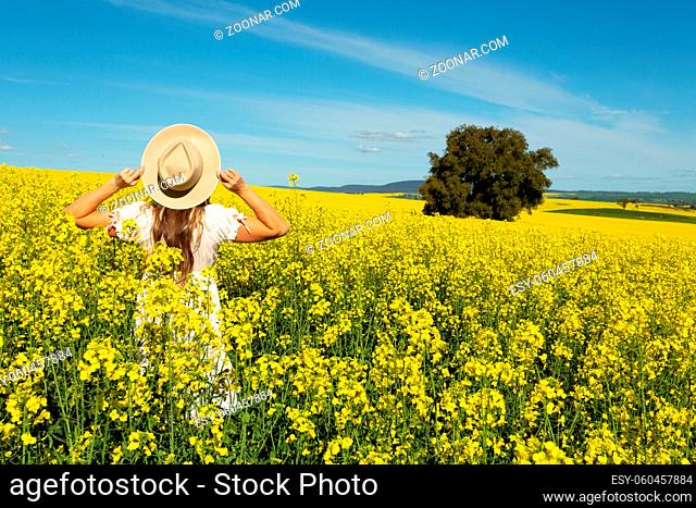 Woman in white dress in field of golden canola flowering in spring in the rural fields of Australia