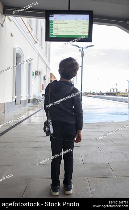 Child boy at railway station looking to departure monitor. Travel on train with children concept