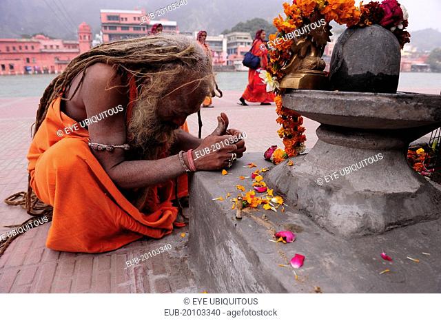 Saddhu praying at shrine draped with flower garland offerings during Kumbh Mela Indias biggest religious festival where many different traditions of Hinduism...