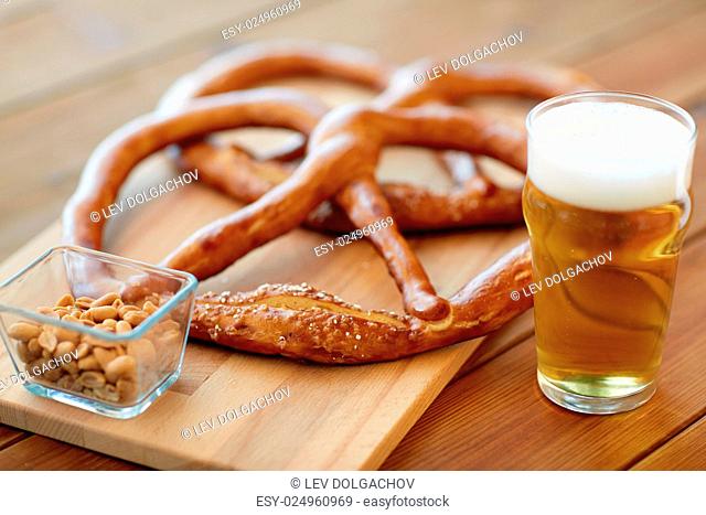 food, baking, cooking and pastry concept - close up of beer in glass, pretzels and peanuts on wooden table