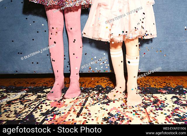 Legs of girls standing on floor covered with confetti