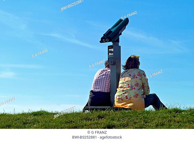 two persons sitting next coin telescope on dyke, Germany, Lower Saxony, Neuharlingersiel