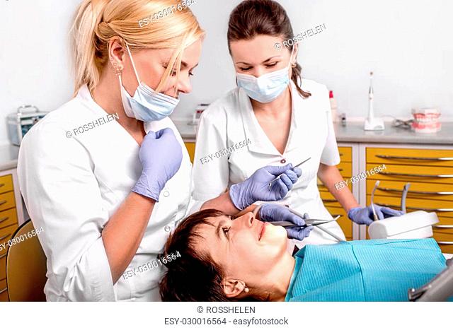 Senior woman on the operation in the dental office. Dentist with assistant putting dental seal