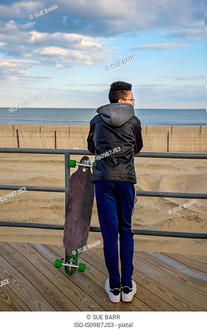 Young boy leaning against railings, looking at view, skateboard beside him, Asbury, New Jersey, USA
