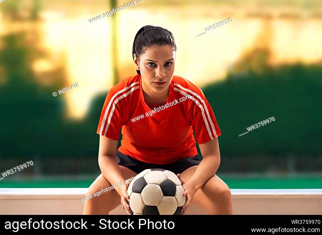 A YOUNG WOMAN PLAYER SITTING WHILE HOLDING FOOTBALL