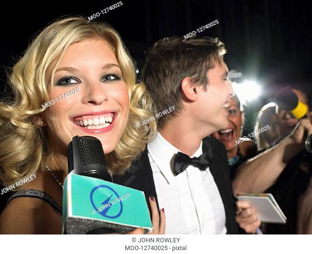 Woman talking into microphone man behind with paparazzi
