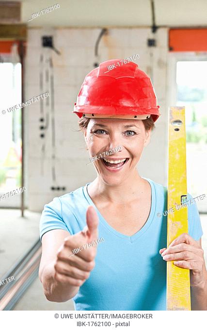 Craftswoman with hard hat and level giving a thumbs up