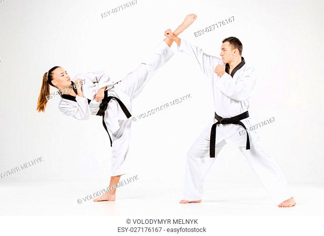 The karate girl and boy in white kimono and black belt training karate over gray background