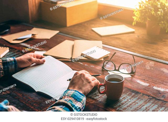 Making some notes. Close-up image of man writing in notebook while sitting at the rustic wooden table