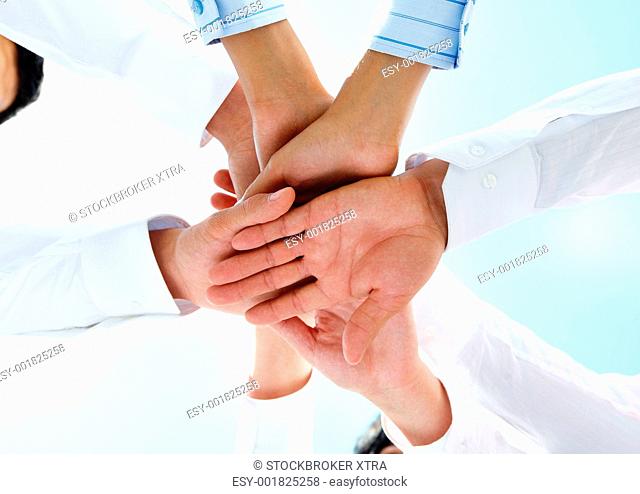 Bottom view of people hands holding together on a sky background
