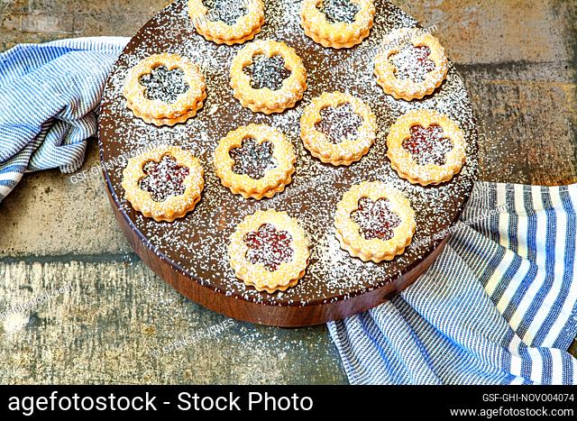 High angle view of Linzer tarts dusted with powdered sugar on round wood board with blue towel