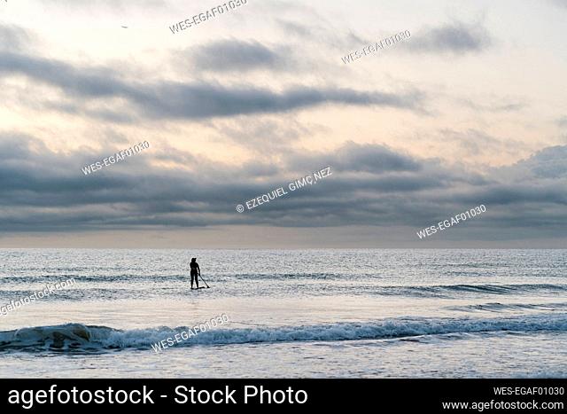 Woman paddleboarding on sea against sky during dawn