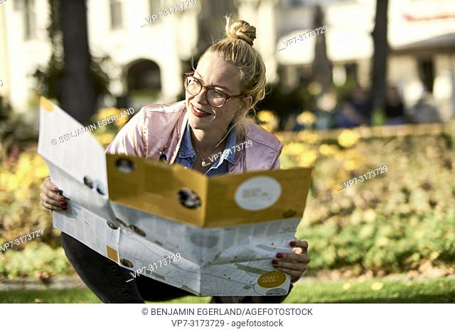 Woman with city guide map crouching on meadow in park, in Berlin, Germany