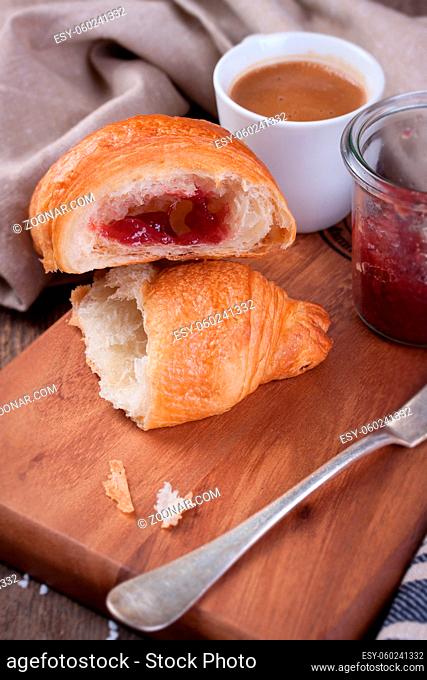 Closeup of croissant with jam and coffee on a wooden background