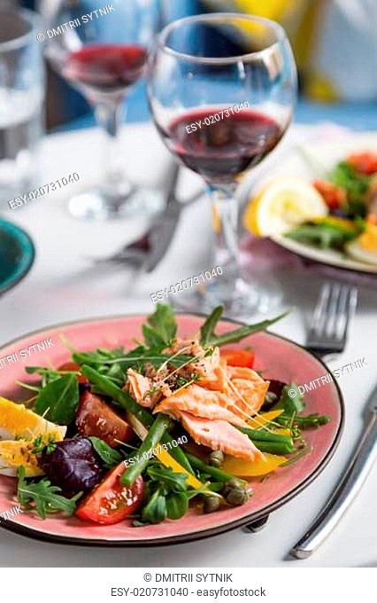 salad with salmon and verdure in plate on table with blue chair background