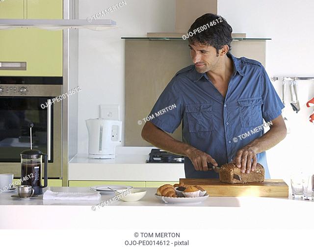 Man in kitchen slicing bread with coffee and baked goods