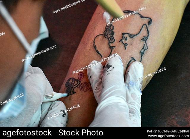 02 March 2021, Myanmar, Nyaung Shwe: A tattoo artist works on a portrait of Aung San Suu Kyi, ousted head of government of Myanmar