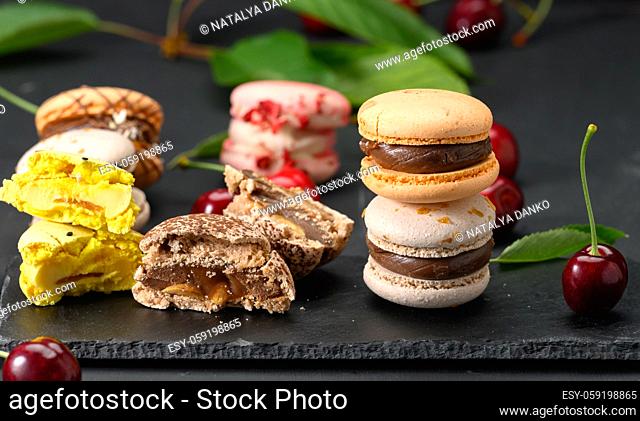 stack of multicolored macarons and ripe red cherries on black wooden background, close up