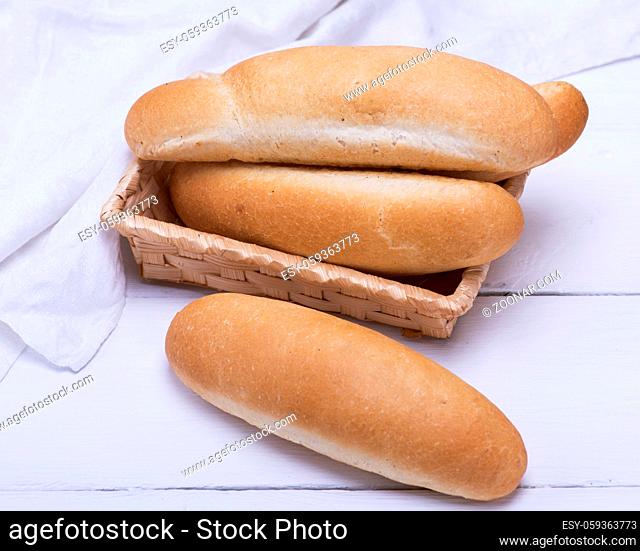 buns of white wheat flour in a wicker basket on a white wooden table, top view