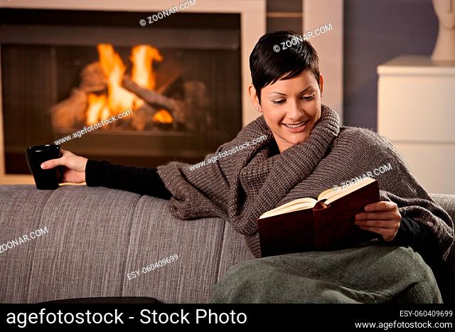 Woman sitting on sofa at home on a cold winter day, reading book